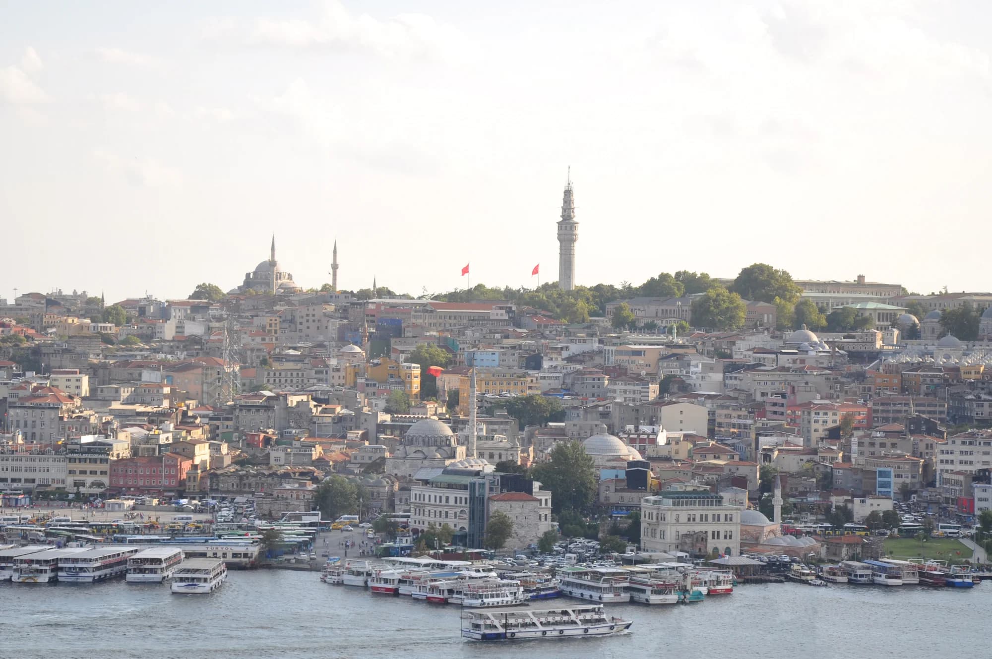 Istiklal Caddesi at dusk — the historic red tram rolling through crowds of pedestrians, the facades of 19th-century apartment blocks illuminated, the neon signs of restaurants and cinemas beginning to glow against a deepening sky
