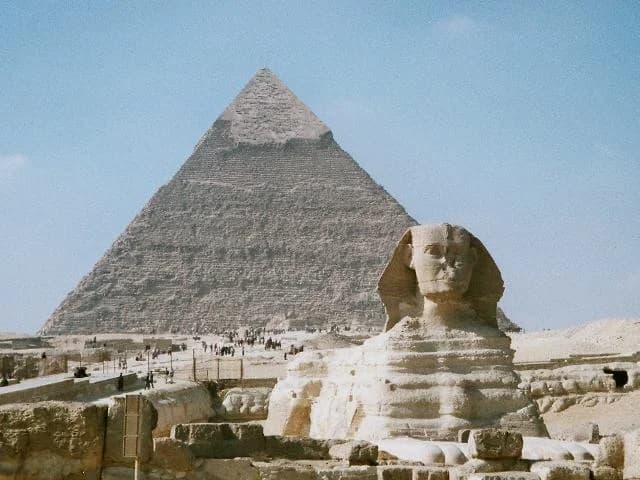 The Great Pyramid of Khufu at dawn — the last surviving Wonder of the Ancient World rising from the Giza plateau, the limestone catching the first light of the Egyptian sun, the desert stretching to the western horizon, the city of Cairo a distant presence on the eastern skyline, five thousand years of history compressed into a single, perfect geometry