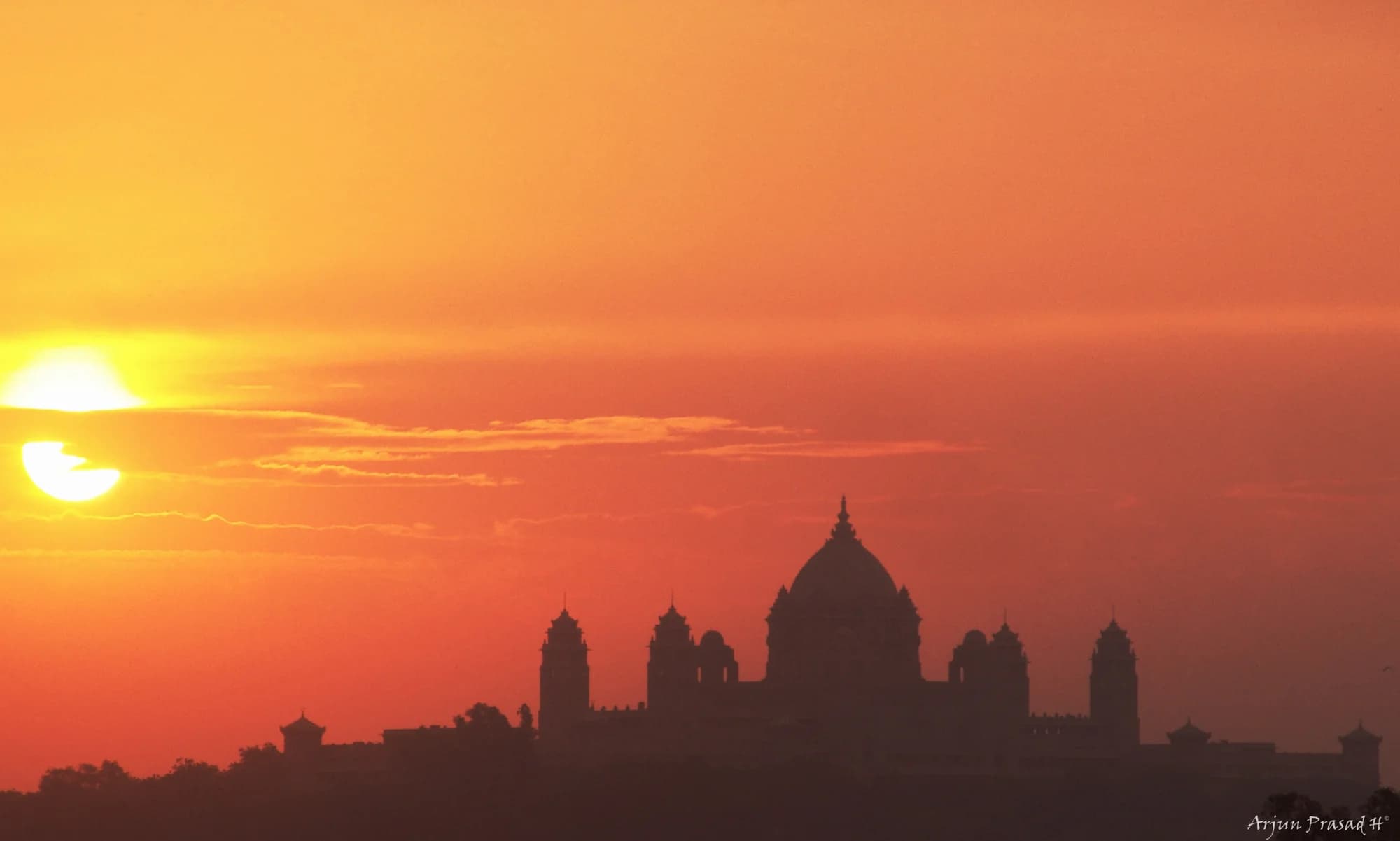 Sunset aperitifs on the palace terrace — a dedicated butler arranges champagne and canapés as the sun descends behind Mehrangarh Fort, turning the desert sky through every shade of orange, rose, and violet