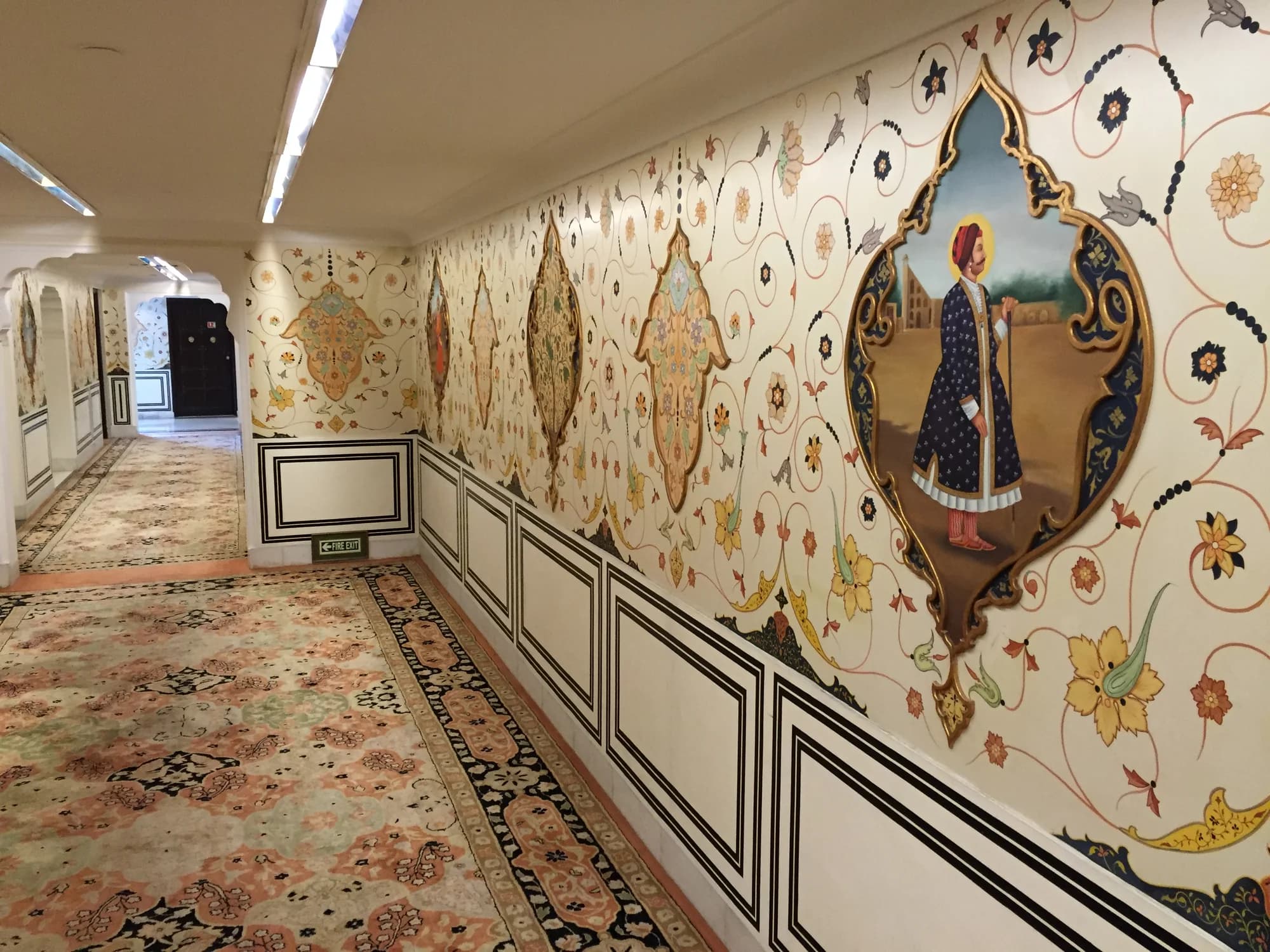 The central durbar hall at Rambagh Palace — crystal chandeliers, gilded mirrors, and a ceiling that took artisans fourteen years to complete, every square inch covered in hand-painted floral motifs in gold leaf