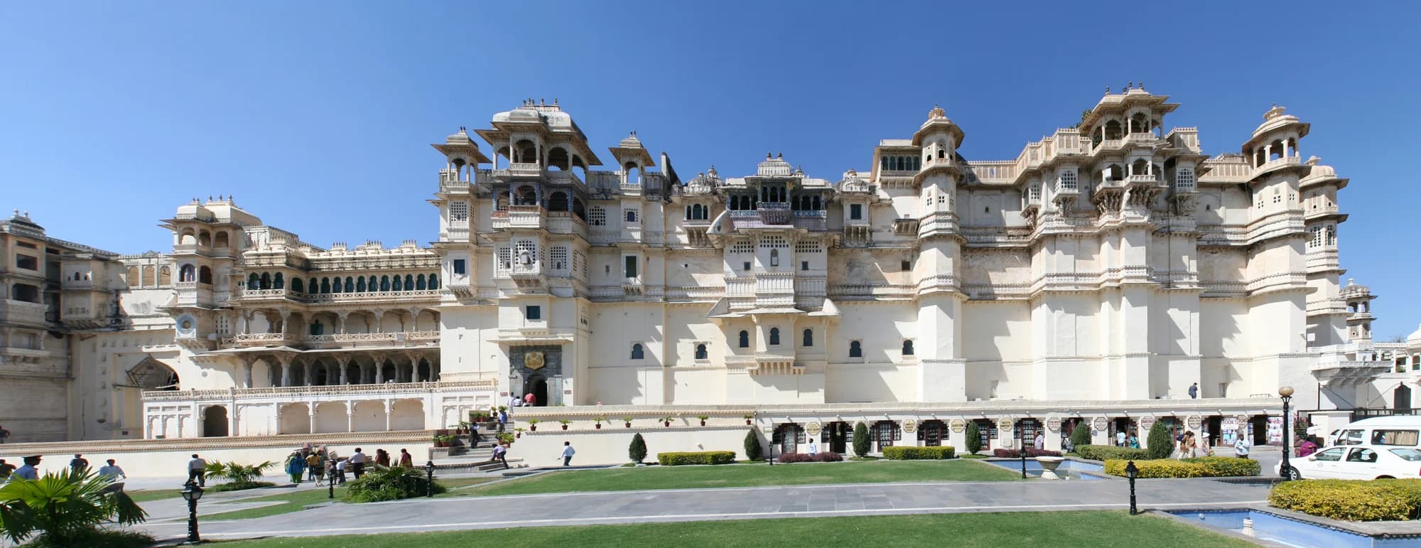 Devi Garh at dawn — the all-white marble and local stone facade of an 18th-century fort palace rising from the Aravalli Hills, the village of Delwara visible in the valley below, the morning mist softening the rugged landscape