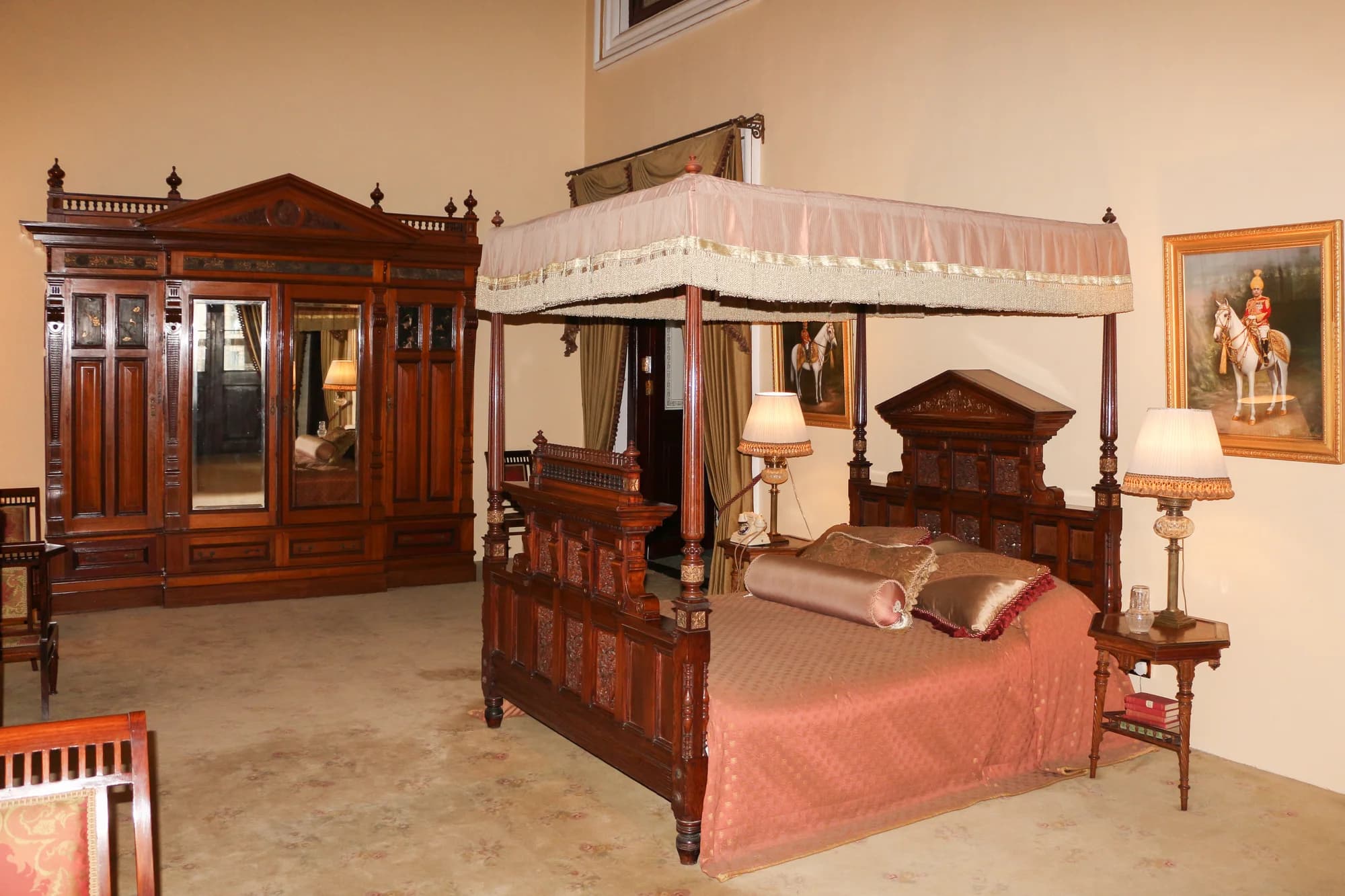 The Nizam Suite bedroom — a carved four-poster bed beneath a frescoed ceiling of the Golconda night sky, French windows opening onto a private balcony with views across Hyderabad to the horizon