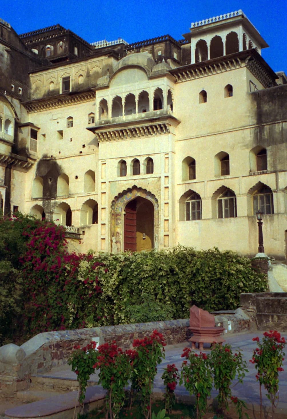 A steep stone staircase at Neemrana — one of 350 steps connecting the palace's twelve levels, worn smooth by five centuries of feet, sunlight filtering through an arched window in the thick stone wall