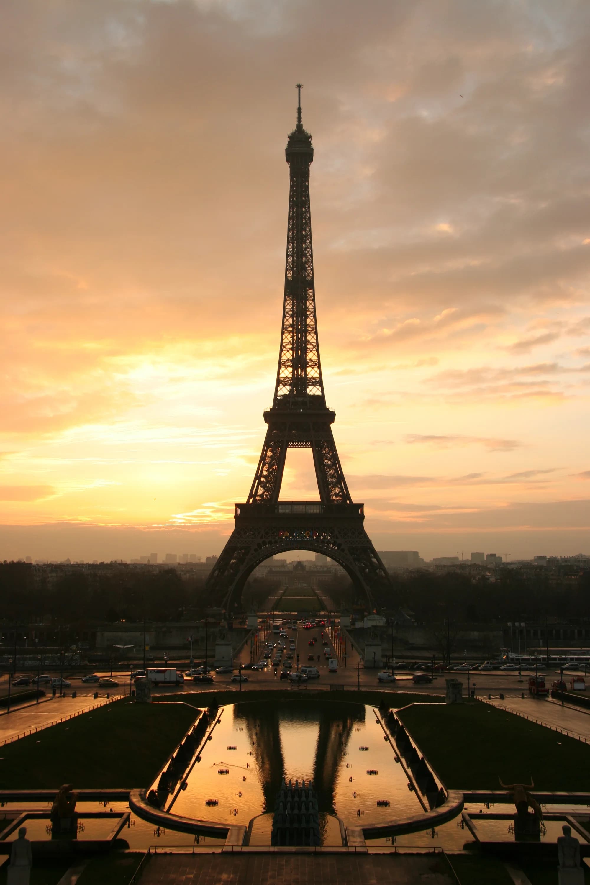 The Eiffel Tower from Trocadéro at blue hour — the Iron Lady illuminated against a deepening Parisian sky, the fountains of the Jardins du Trocadéro dancing in the foreground, the Seine a dark ribbon winding through the city of light