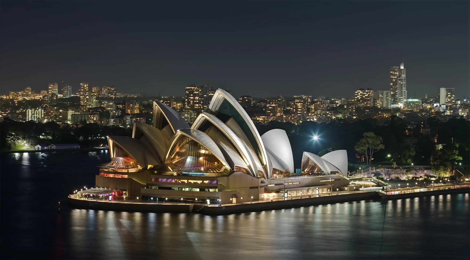 The interior of the Sydney Opera House Concert Hall — soaring ribs of birch ply and concrete rising to the vaulted ceiling, the Grand Organ with its 10,000 pipes gleaming in warm light, a symphony orchestra tuning before a sold-out evening performance