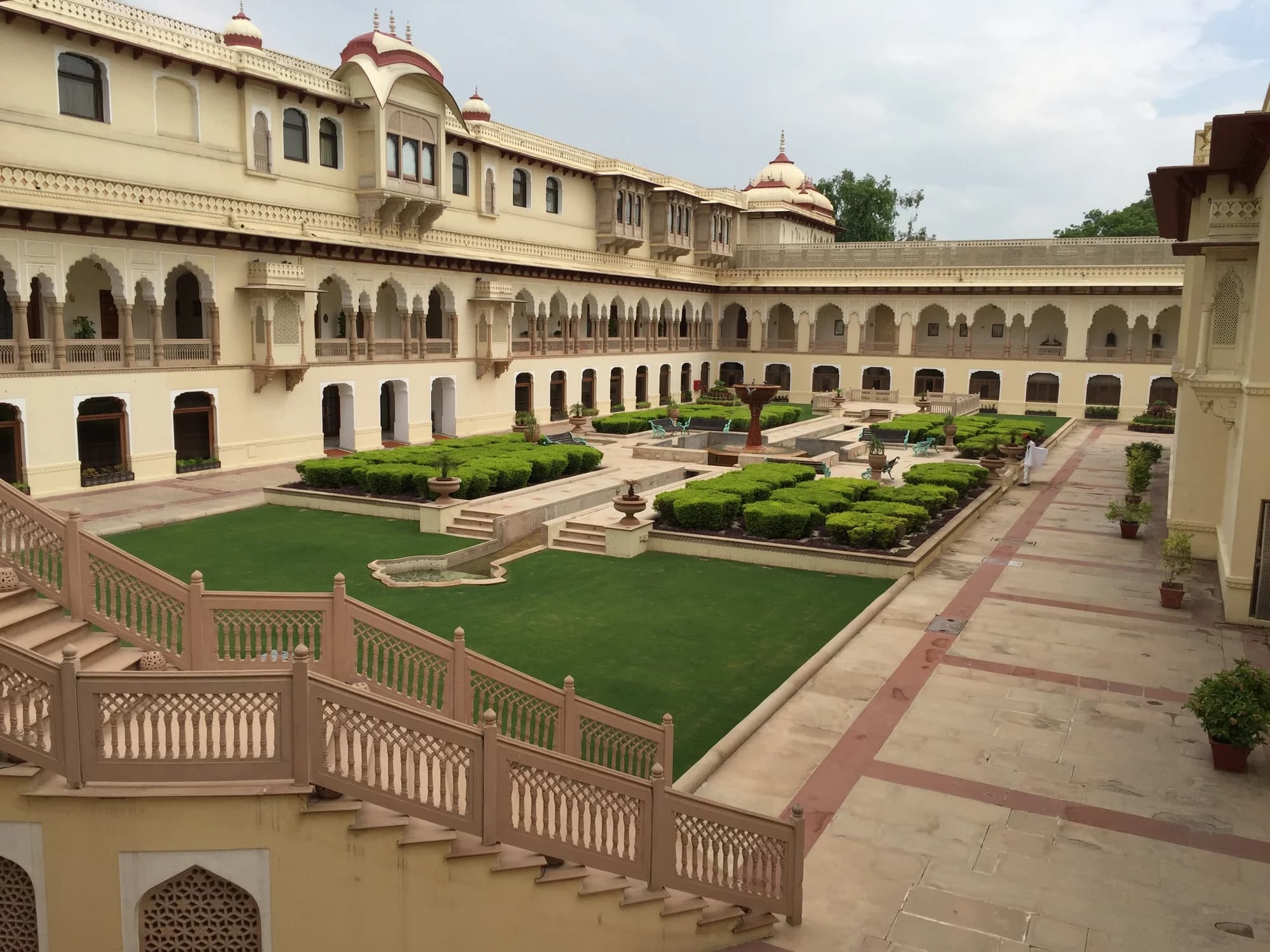 Rambagh Palace Jaipur — the ochre facade catching morning light, peacocks crossing immaculate lawns, the former residence of Maharani Gayatri Devi now one of the world's most celebrated palace hotels, where wellness programming draws on Rajasthani royal traditions
